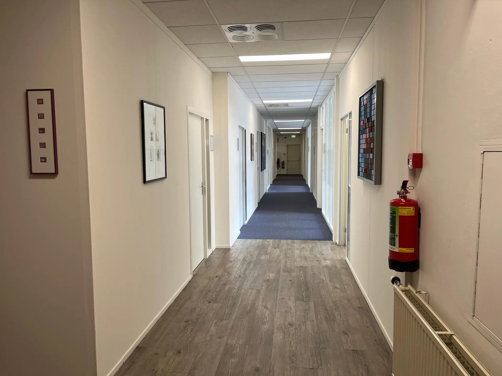 Binnenhal van een kantoorpand aan de Jan van Eycklaan met witte muren, kunst aan de muur en een brandblusser aan de rechterkant.